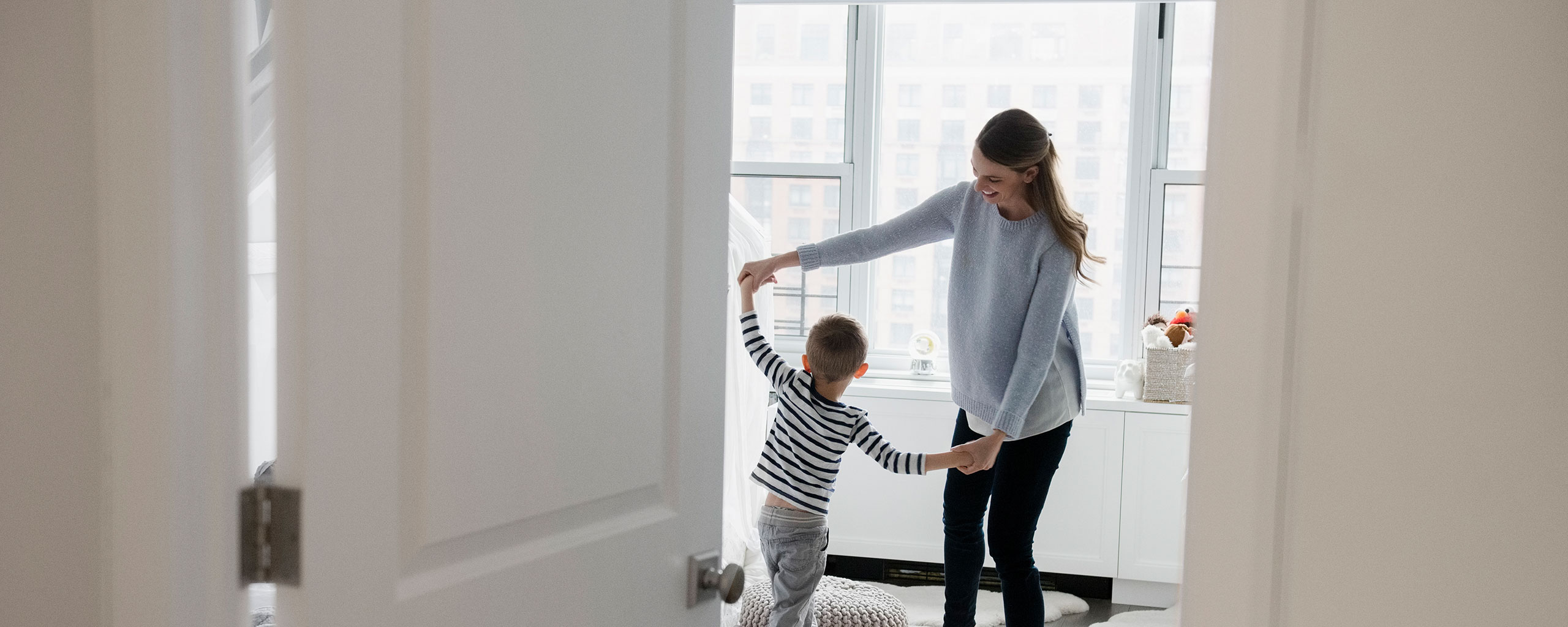 A mother and child hold hands and dance in a home with a minimalist aesthetic.