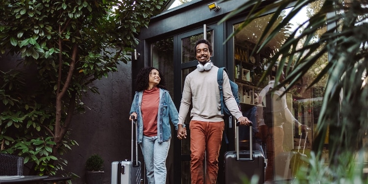 A photo of a couple leaving their home for a vacation, pulling their rolling suitcases behind them.