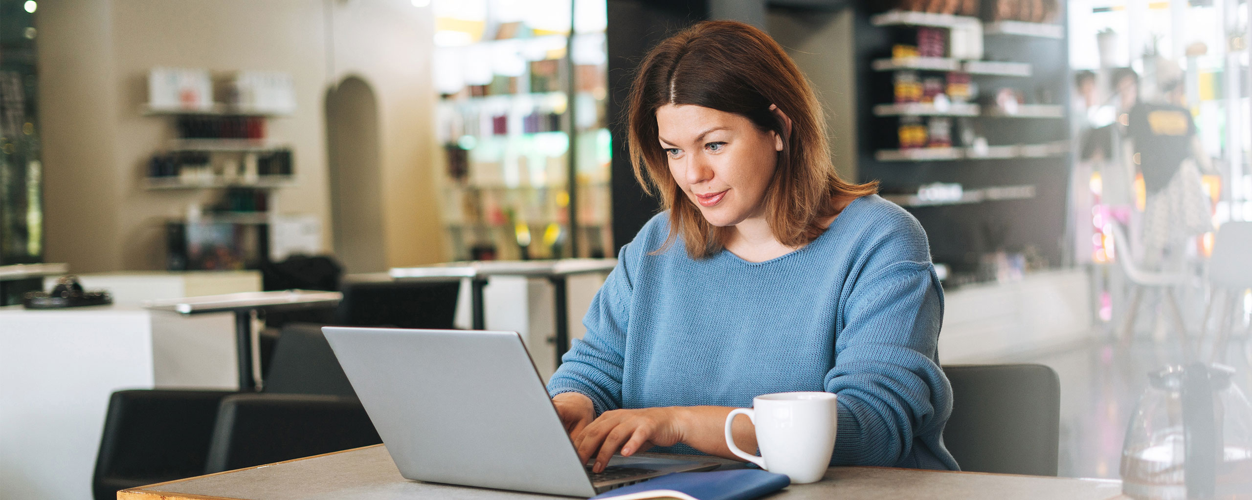 A person looking at their laptop in a coffee shop.
