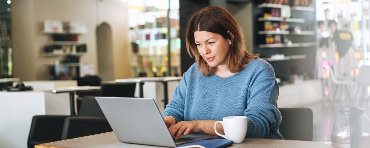 A person looking at their laptop in a coffee shop.