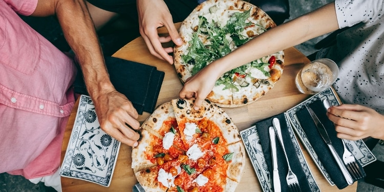 Overhead view of friends at a restaurant reaching for slices of pizza.