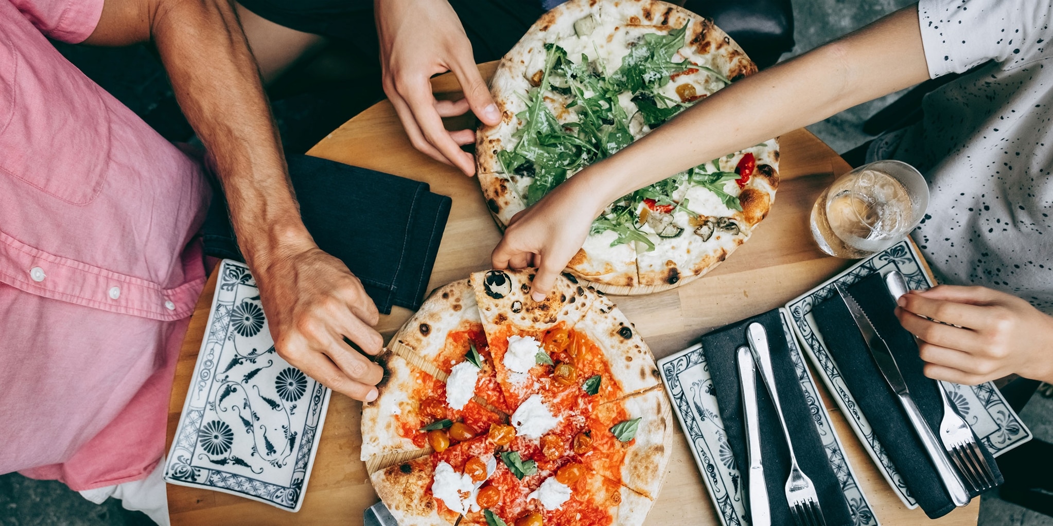 Overhead view of friends reaching for slices of pizza.