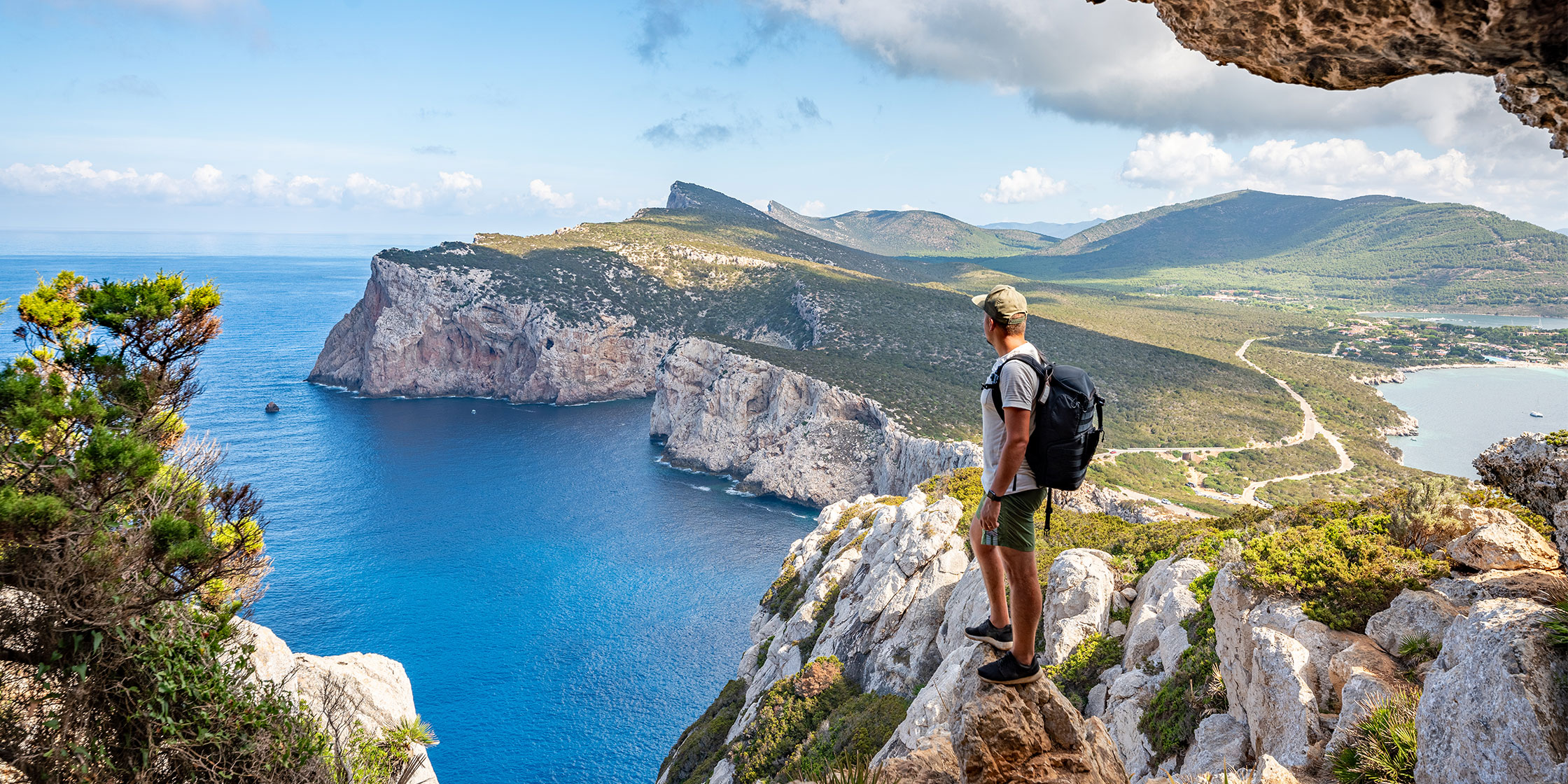 A person on a solo trip stands atop a cliff and looks out at the water.