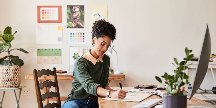 A person sitting at their desk jots down budget numbers in a notebook.