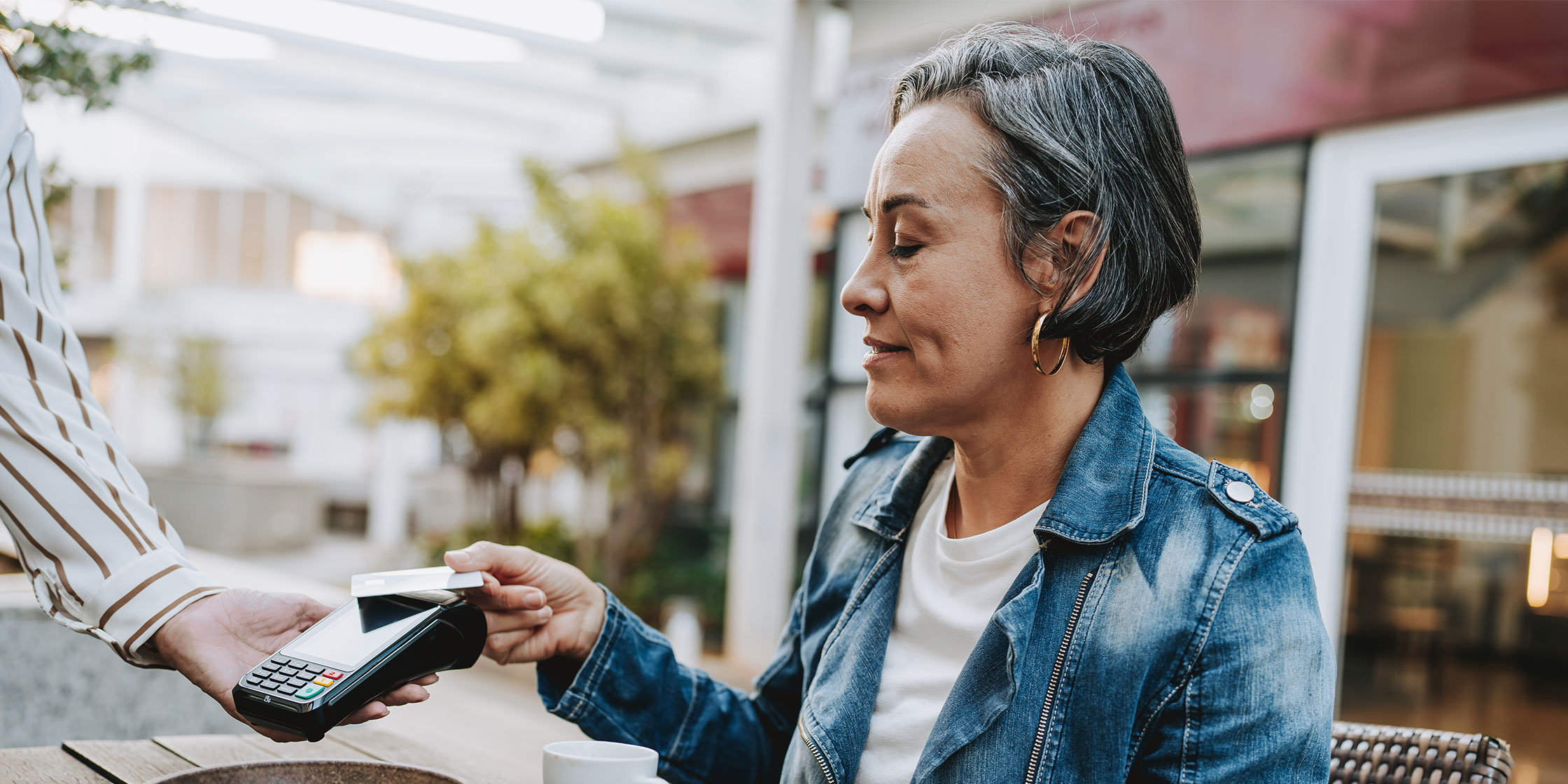 Woman at an outdoor cafe taps her credit card on a wireless terminal, paying her waiter.