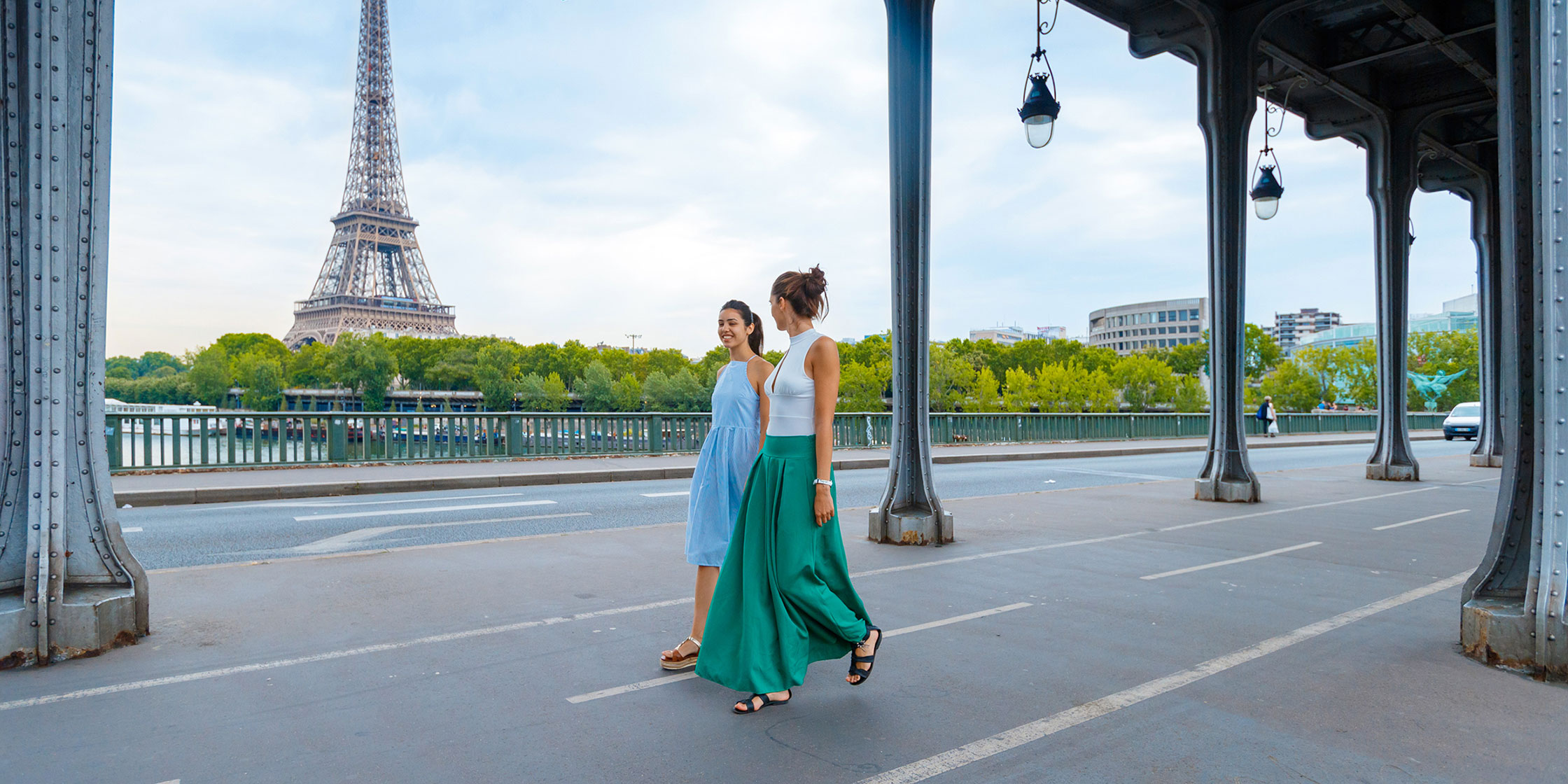 Two tourists walk beneath a bridge during a day out in Paris while the Eiffel Tower sits in the background.