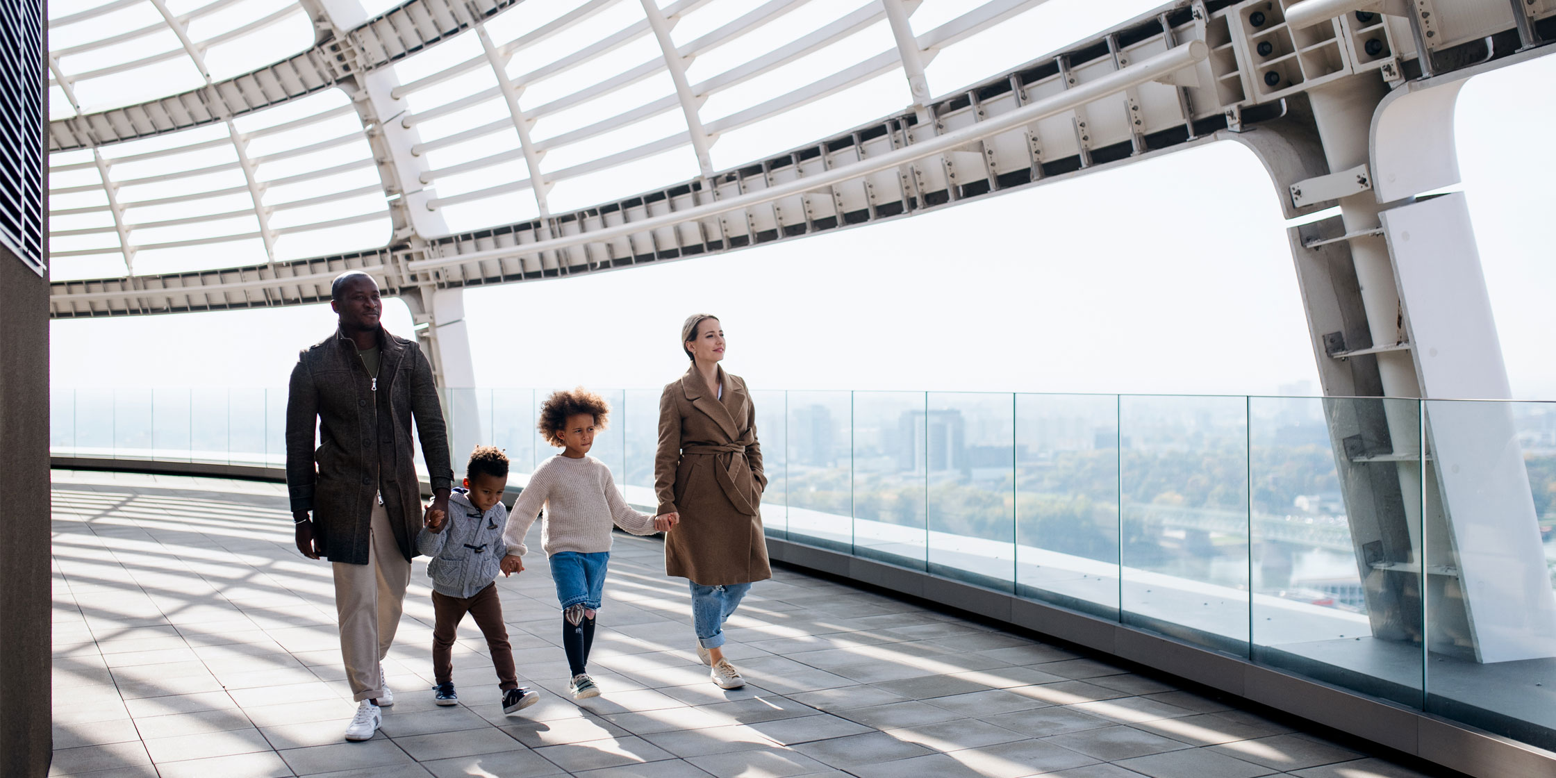 Two adults and two children walk along a city overpass holding hands.
