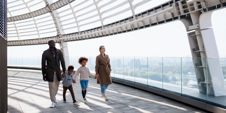 Two adults and two children walk along a city overpass holding hands.