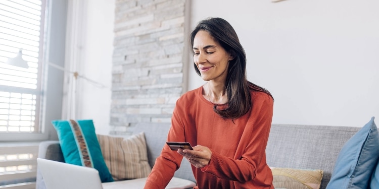 A woman holds a credit card while using her laptop.