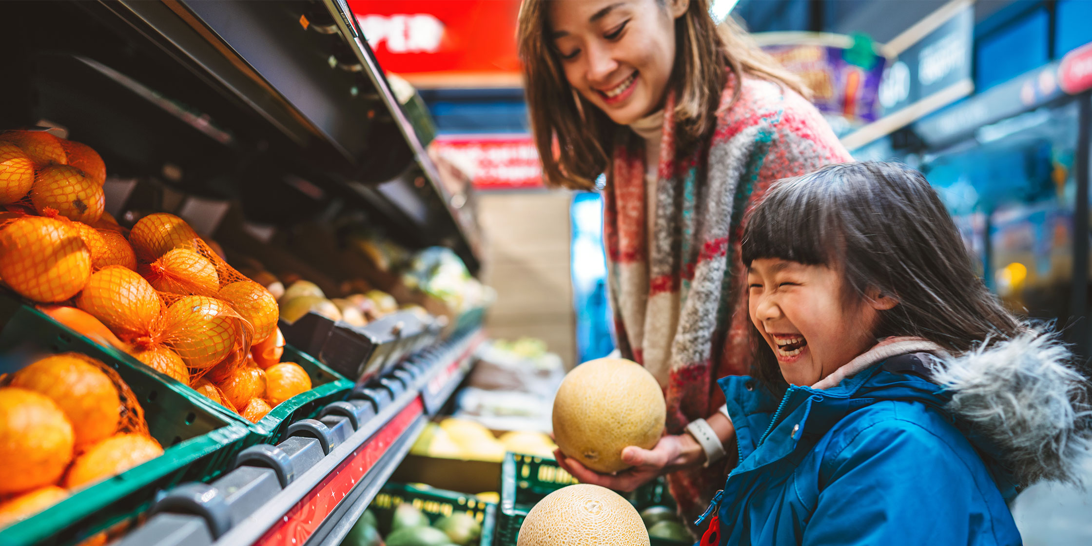 A mother and young daughter laugh while grocery shopping.