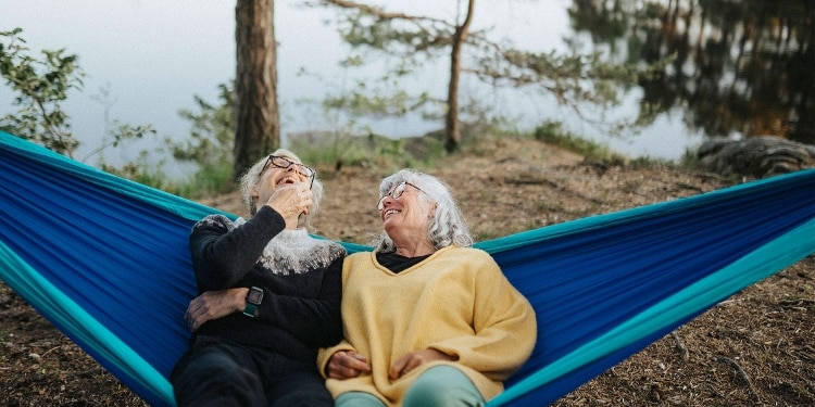 Two people sit in a hammock and laugh together.