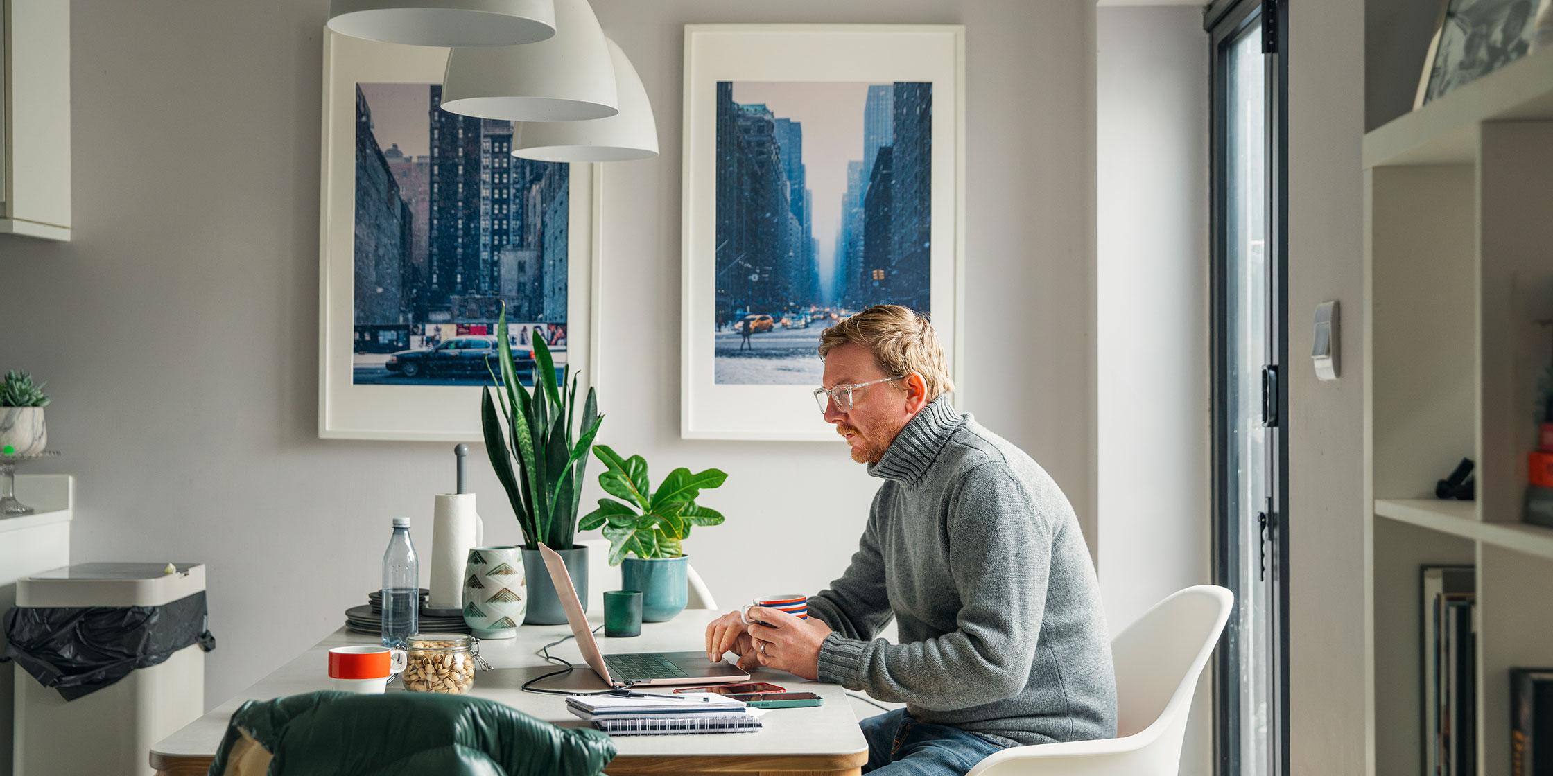 A man sits at a kitchen table looking at his laptop.