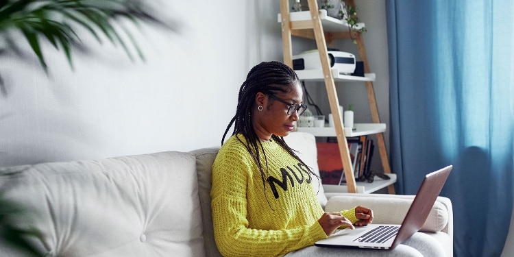 A person sits on their couch and checks their credit scores with a laptop.