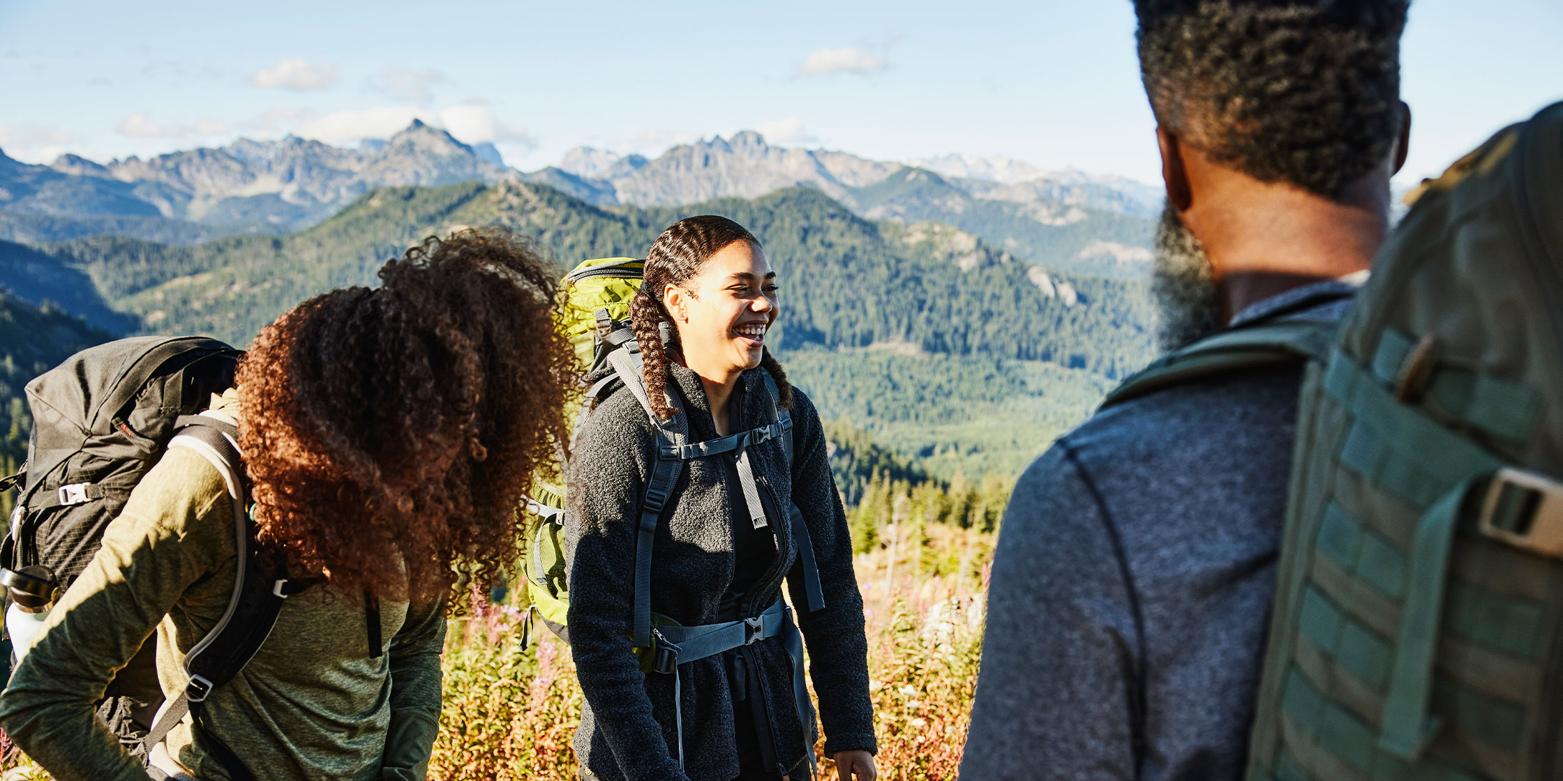 Three teens in the mountains, wearing hiking clothes and carrying backpacks.