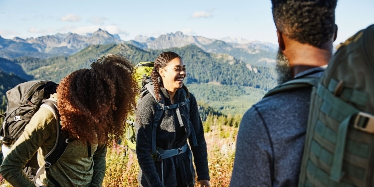 Three teens in the mountains, wearing hiking clothes and carrying backpacks.