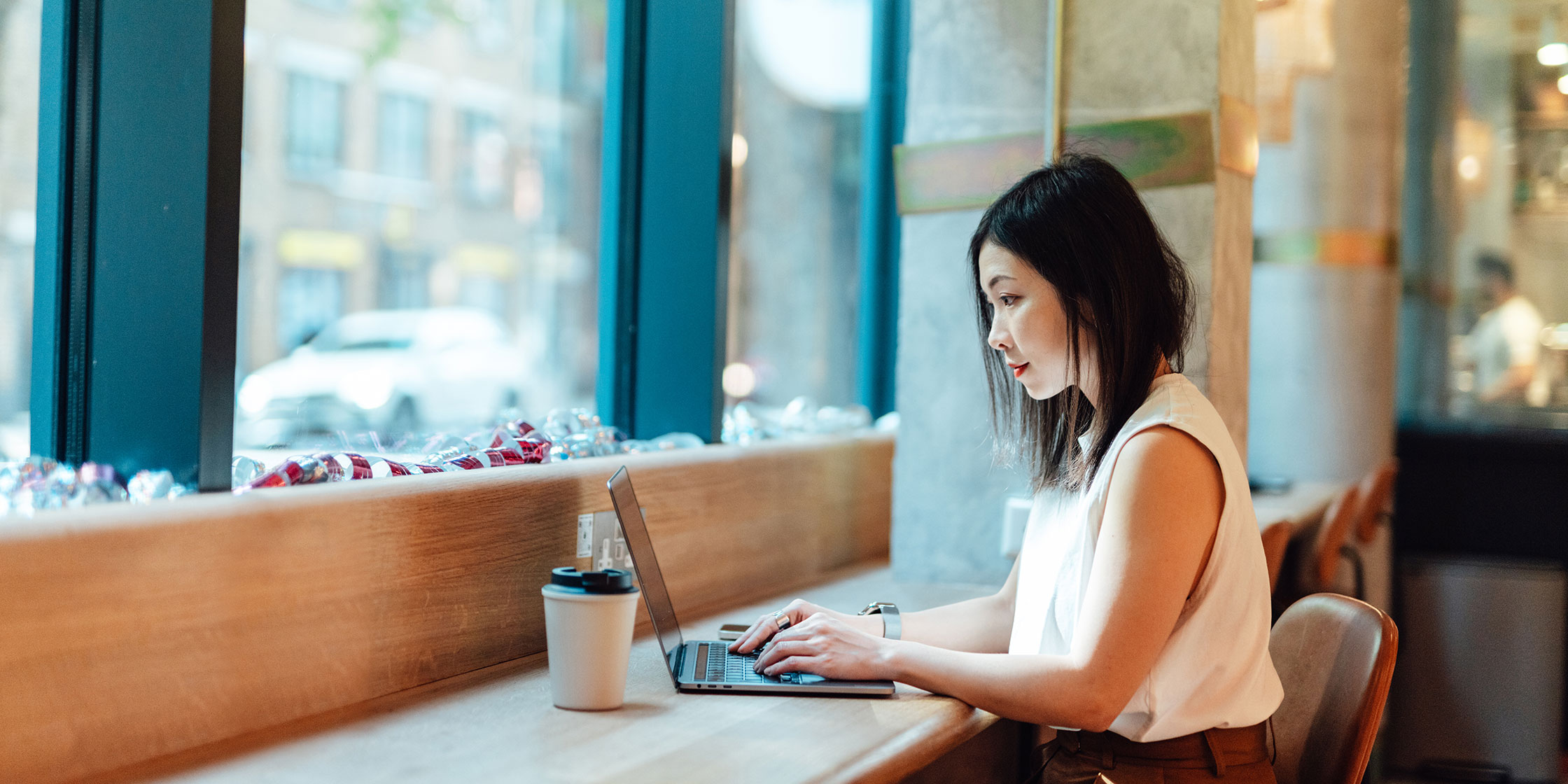A person sits in a coffee shop reading on their laptop.