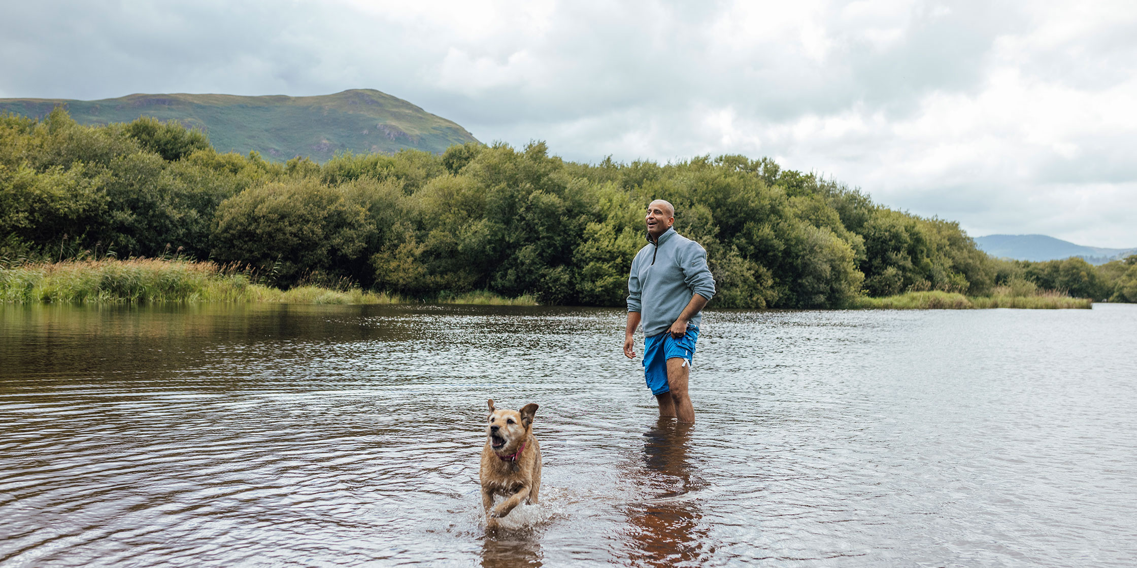 A man and his dog play together in a shallow river.