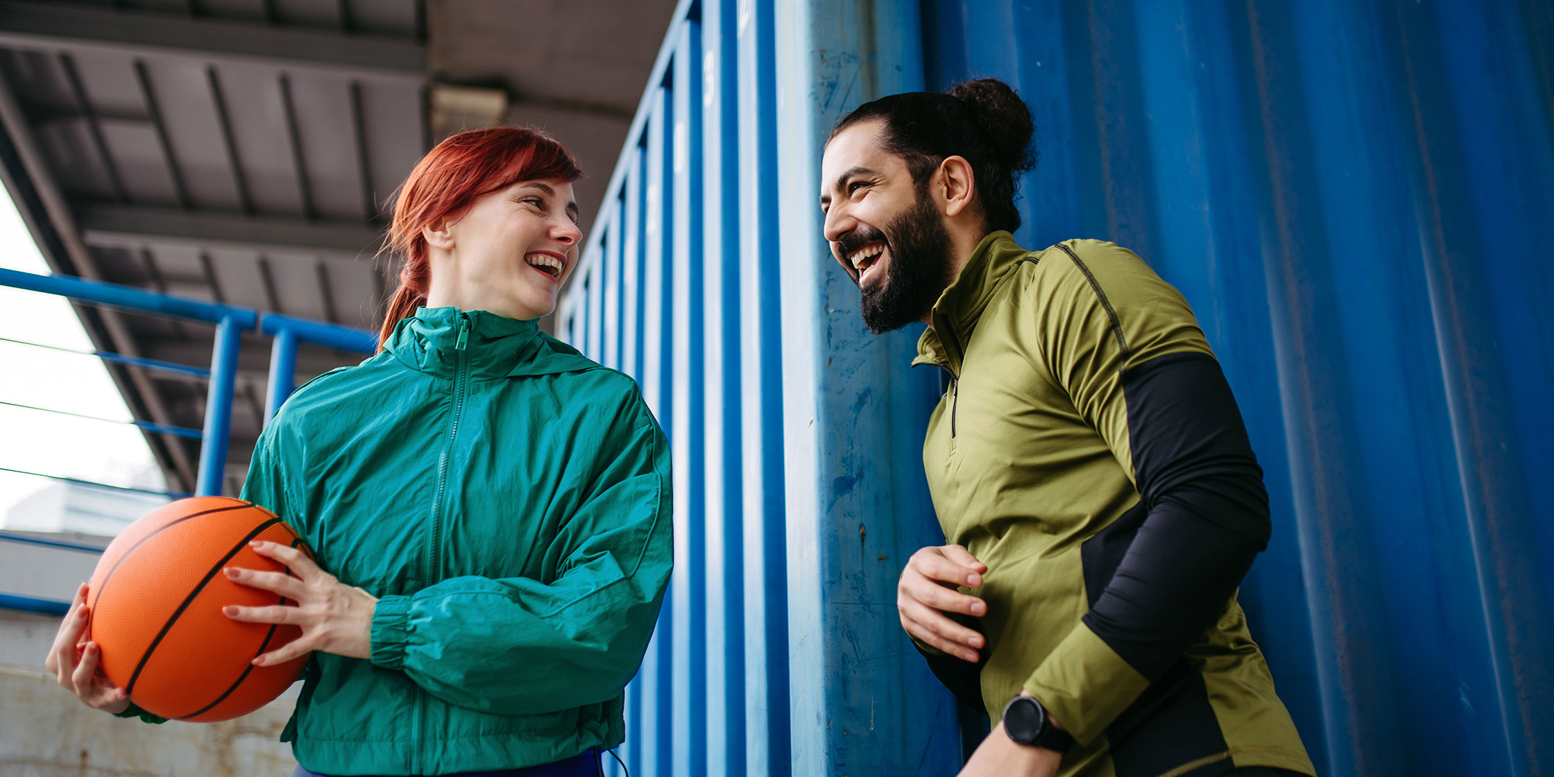 Two smiling people playing basketball outdoors.