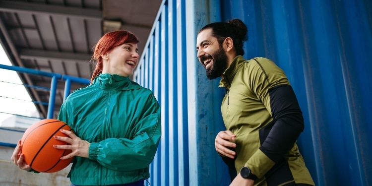 Two smiling people playing basketball outdoors.