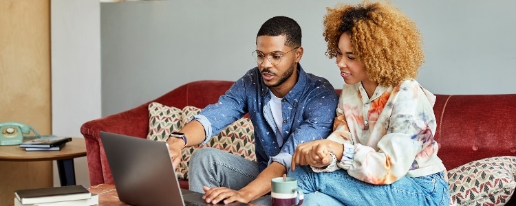 Two people sitting on a couch and using a laptop.