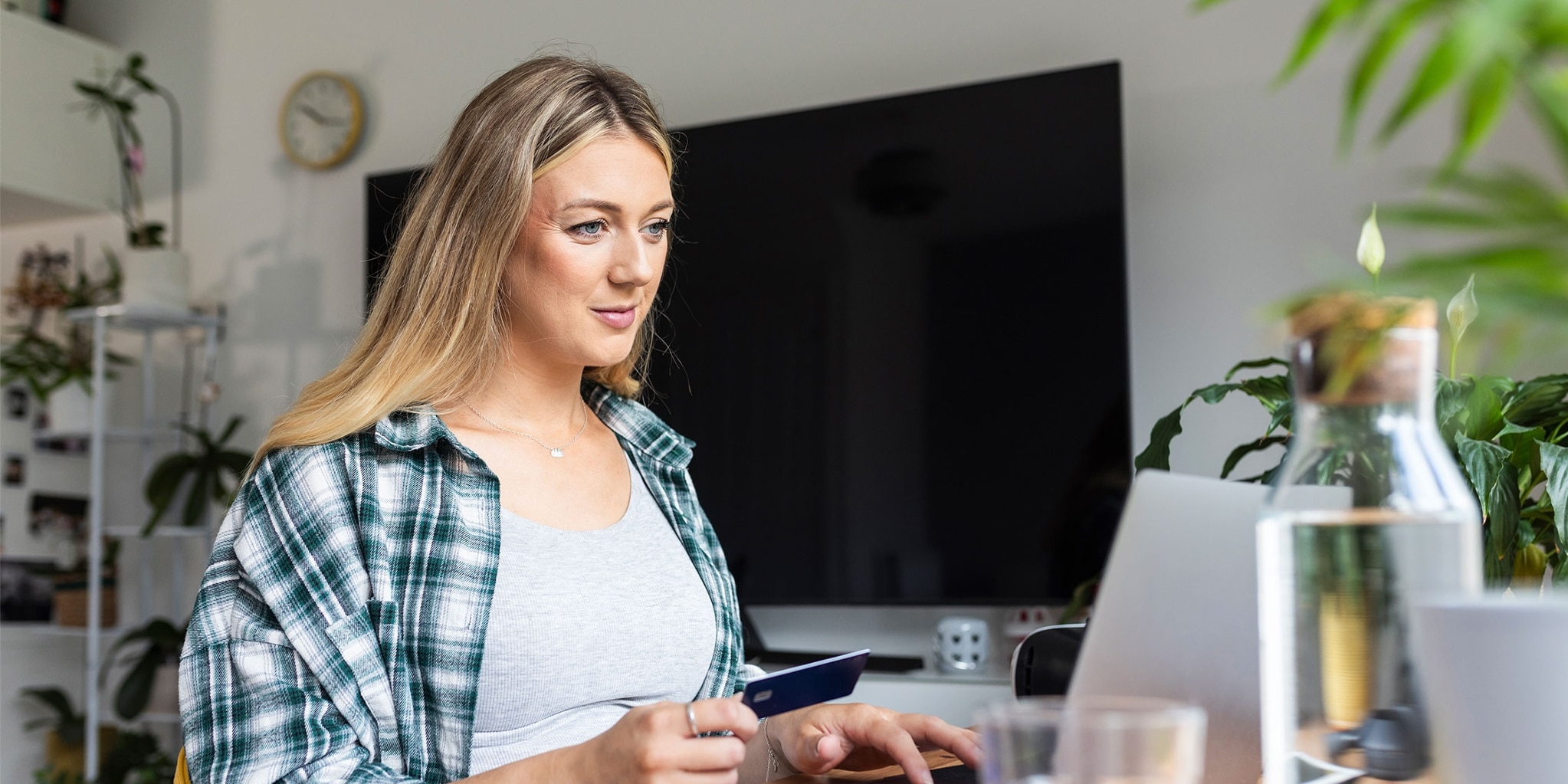 A woman holds a secured credit card and uses a laptop.