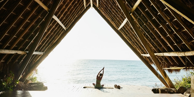 A person doing yoga on a beach under a wooden A-frame structure.