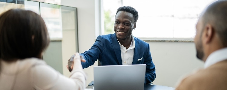 A person shakes hands with two people across a table in an office.