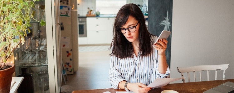 Person holds up phone and piece of paper while looking away.