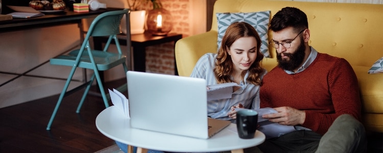 A photo of a couple in their living room, looking on their phone and laptop for information on the standard tax deduction.