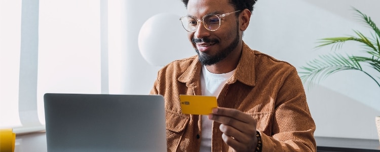 A person in glasses holding their credit card and looking at their laptop.
