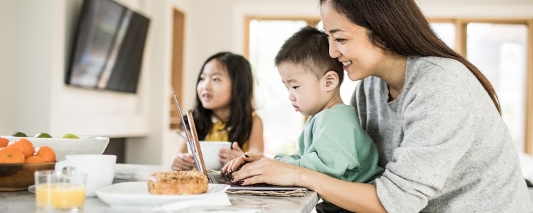 A woman shops online at home with her two kids nearby.