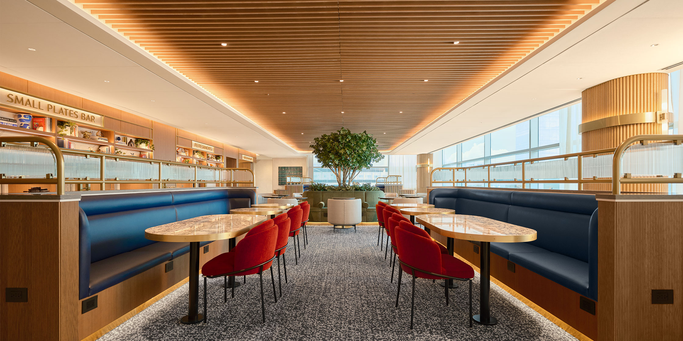 An image of a Capital One Lounge in an airport showing tables, black bench seats and orange chairs.
