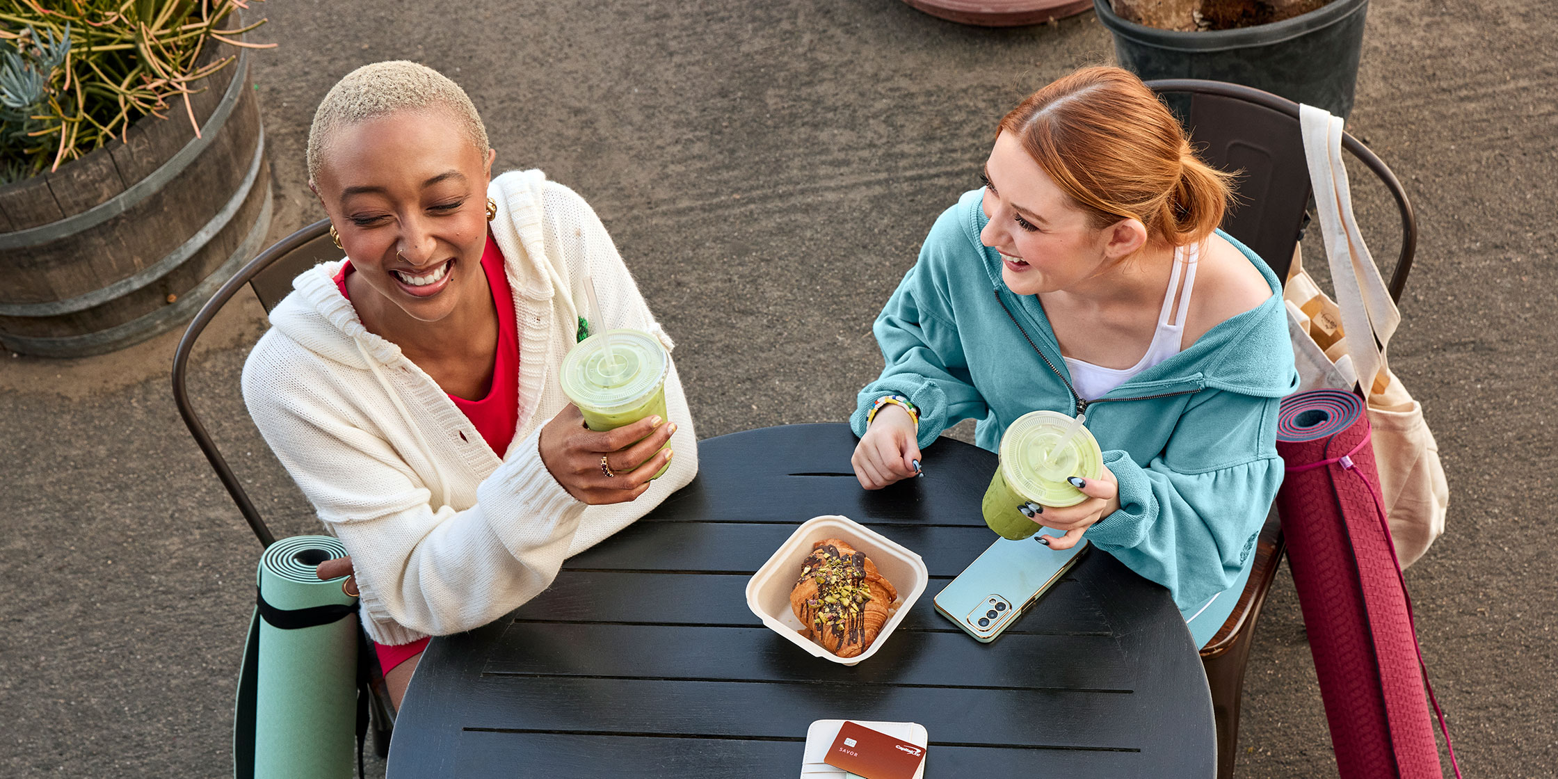 An overhead view of two students with drinks, food and a Savor card at an outdoor cafe table.