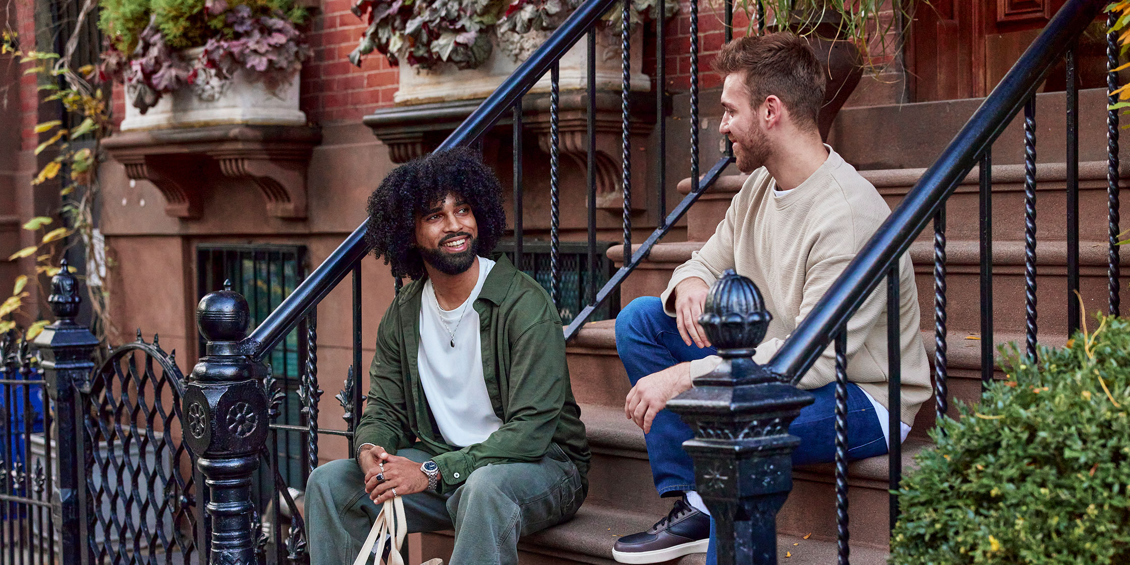 Two men sit and talk on the front stoop of a city brownstone.