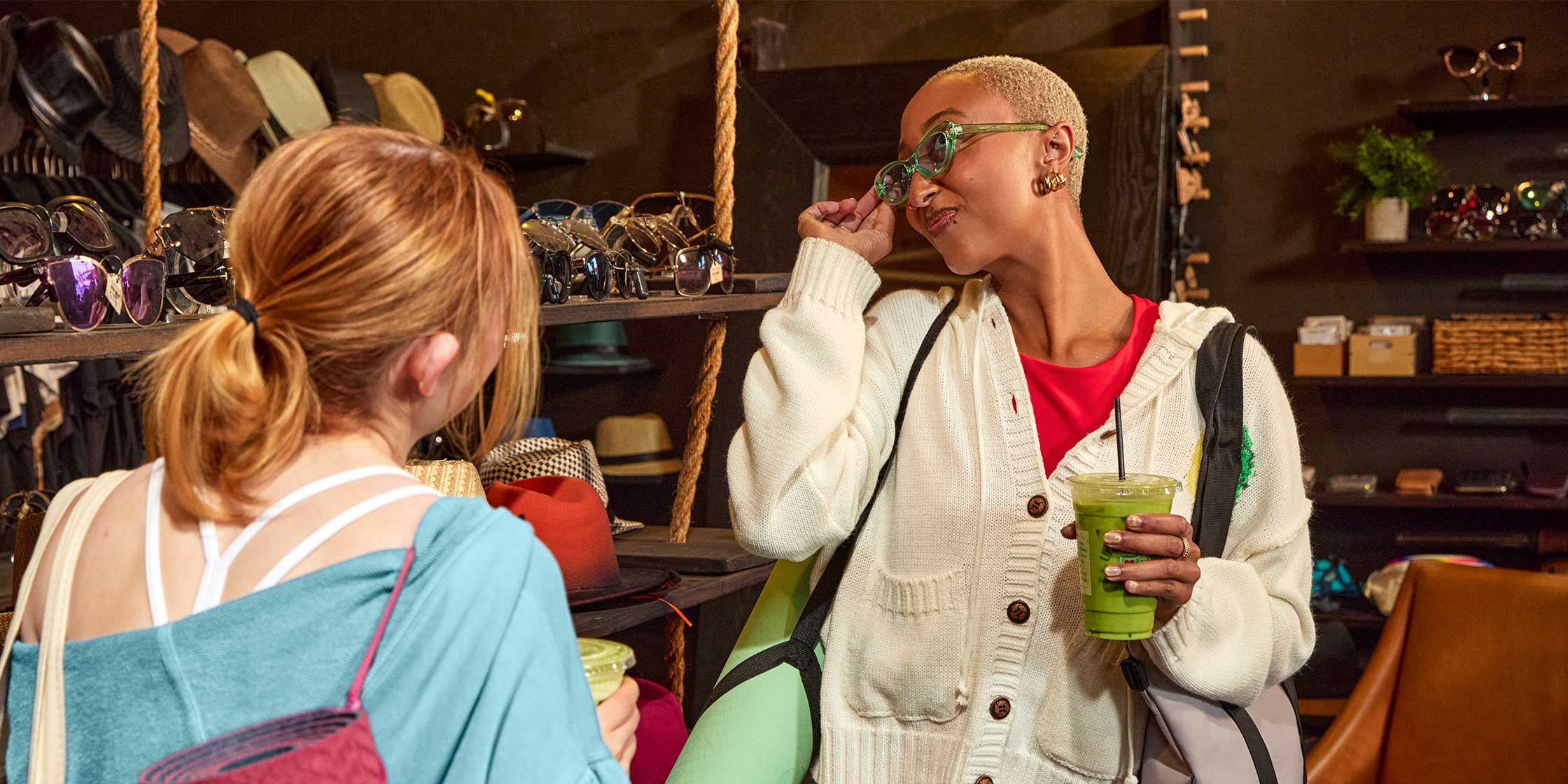 Two students hold drinks and try on sunglasses.