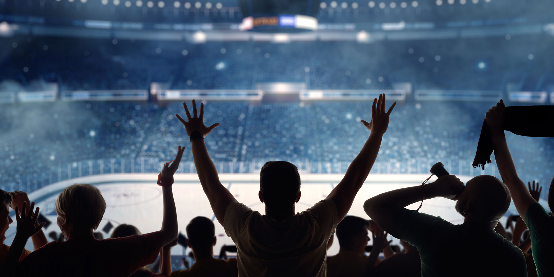 A view of sports fans from behind as they cheer and wave in a large, full arena.