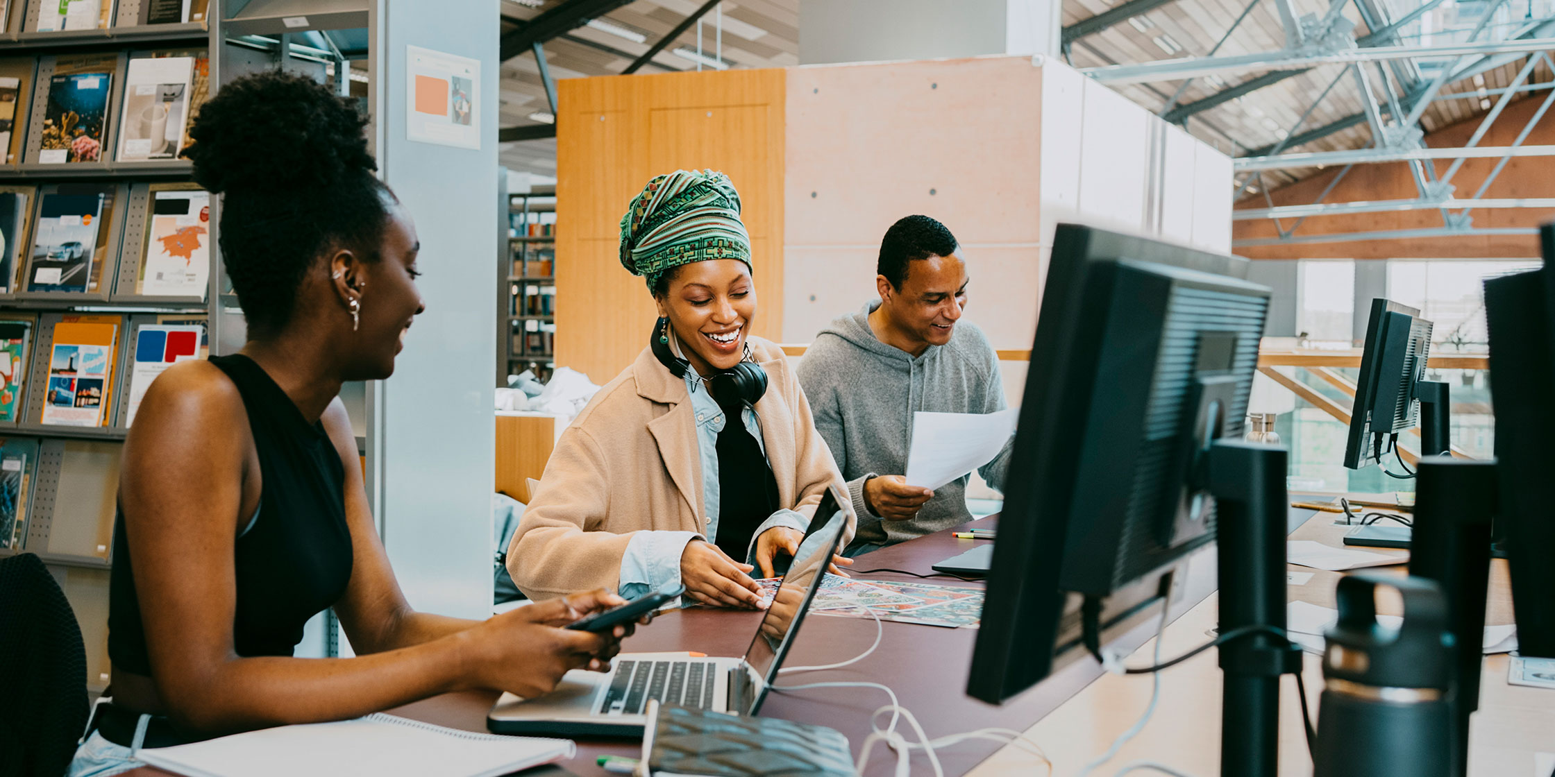 People using laptops and going through papers in a university library.