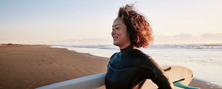 A FIRE movement follower holds a surfboard while they walk on the beach.