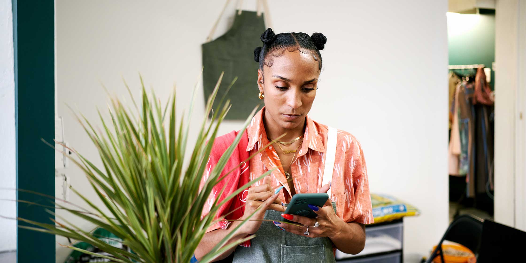 A woman wearing an apron looks serious as she reads a message on her phone.