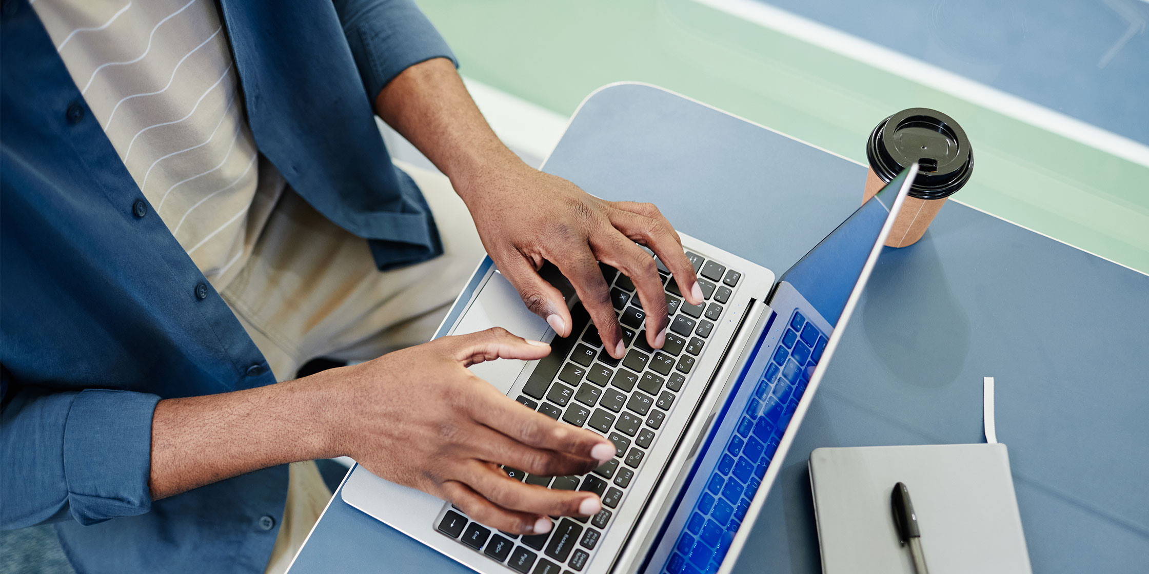Overhead view of a person’s hands typing on a laptop keyboard.