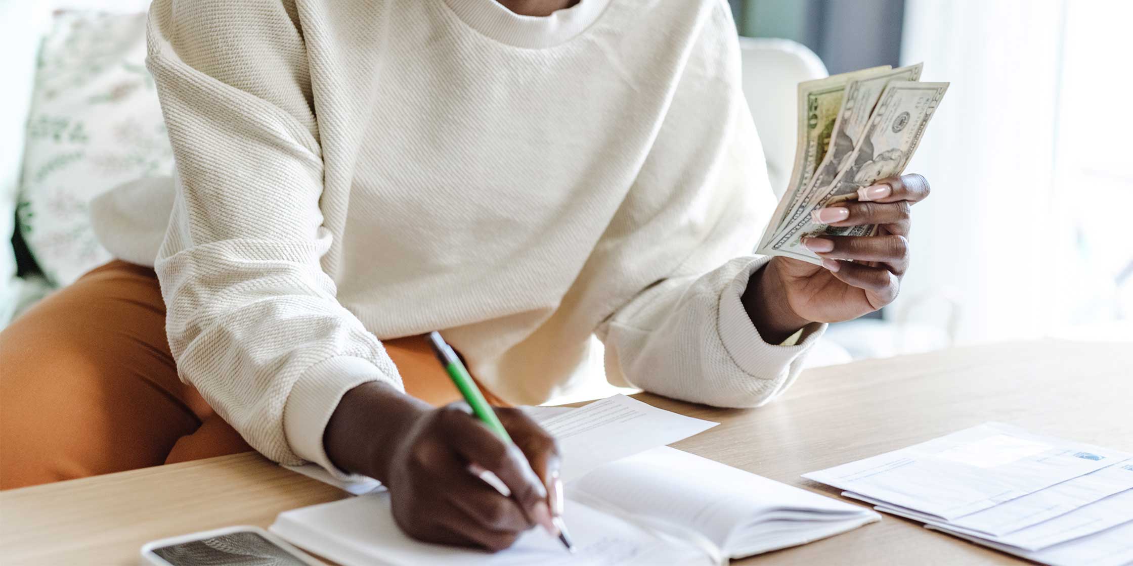 A person holding cash and a pen and using the envelope budget system.