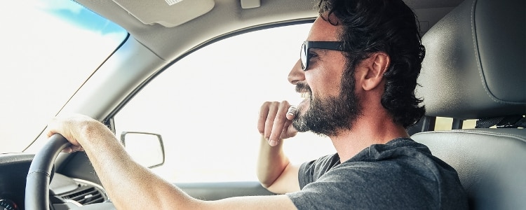 A man wearing sunglasses and driving his car.