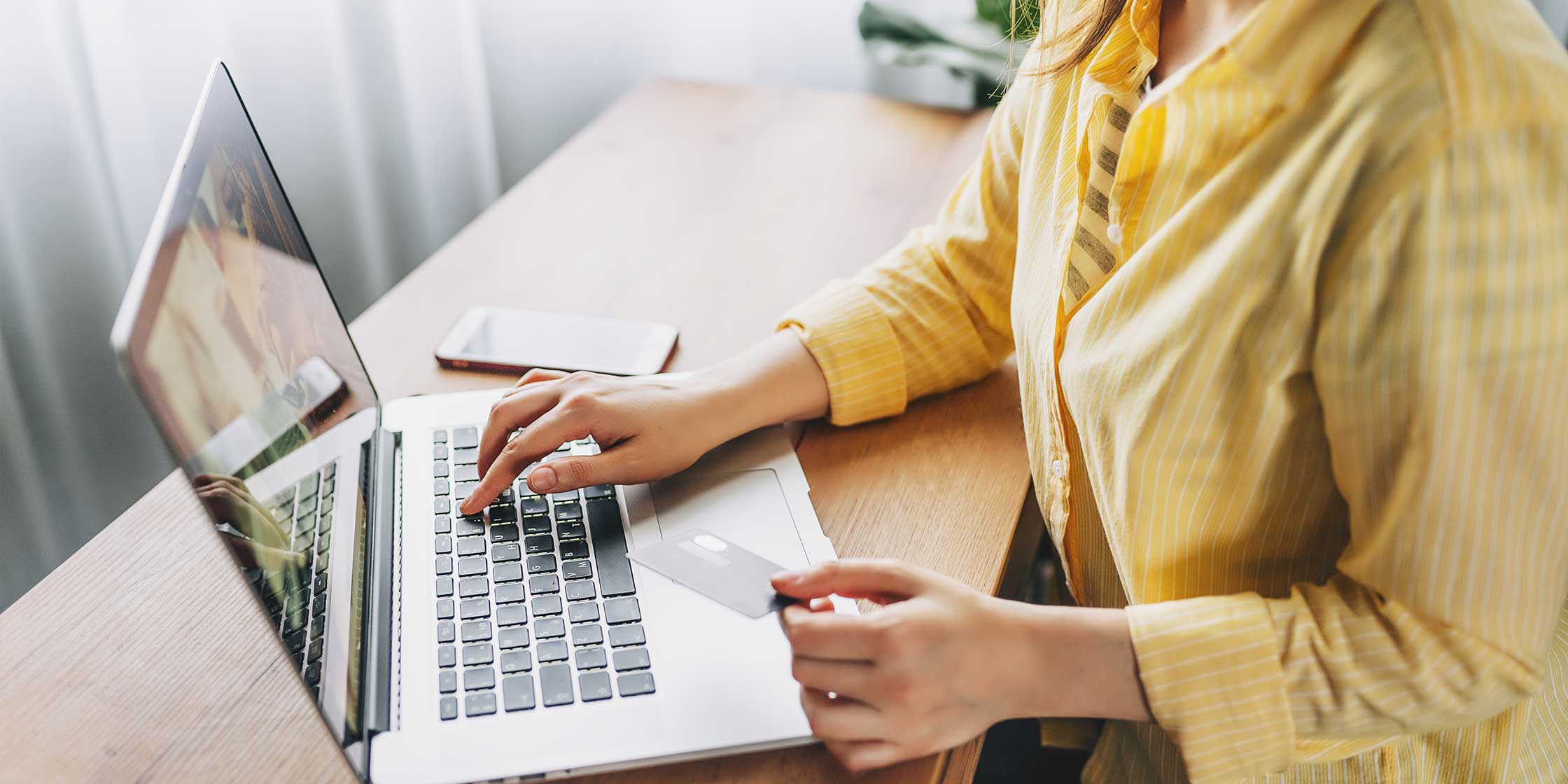 A person holding their credit card while sitting at a desk and typing on a laptop.