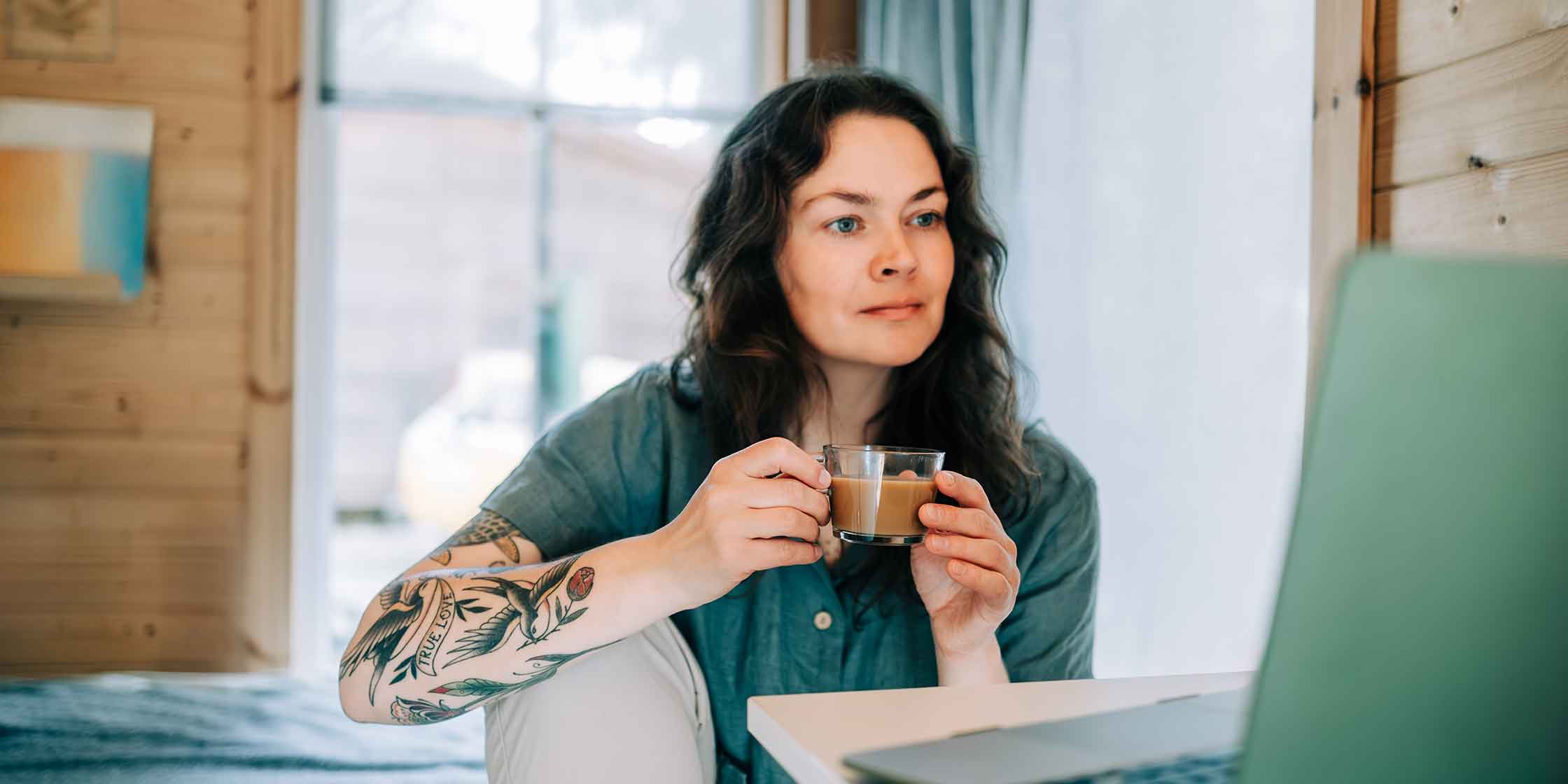 A woman sips coffee while looking at her laptop for information about the Consumer Credit Protection Act.