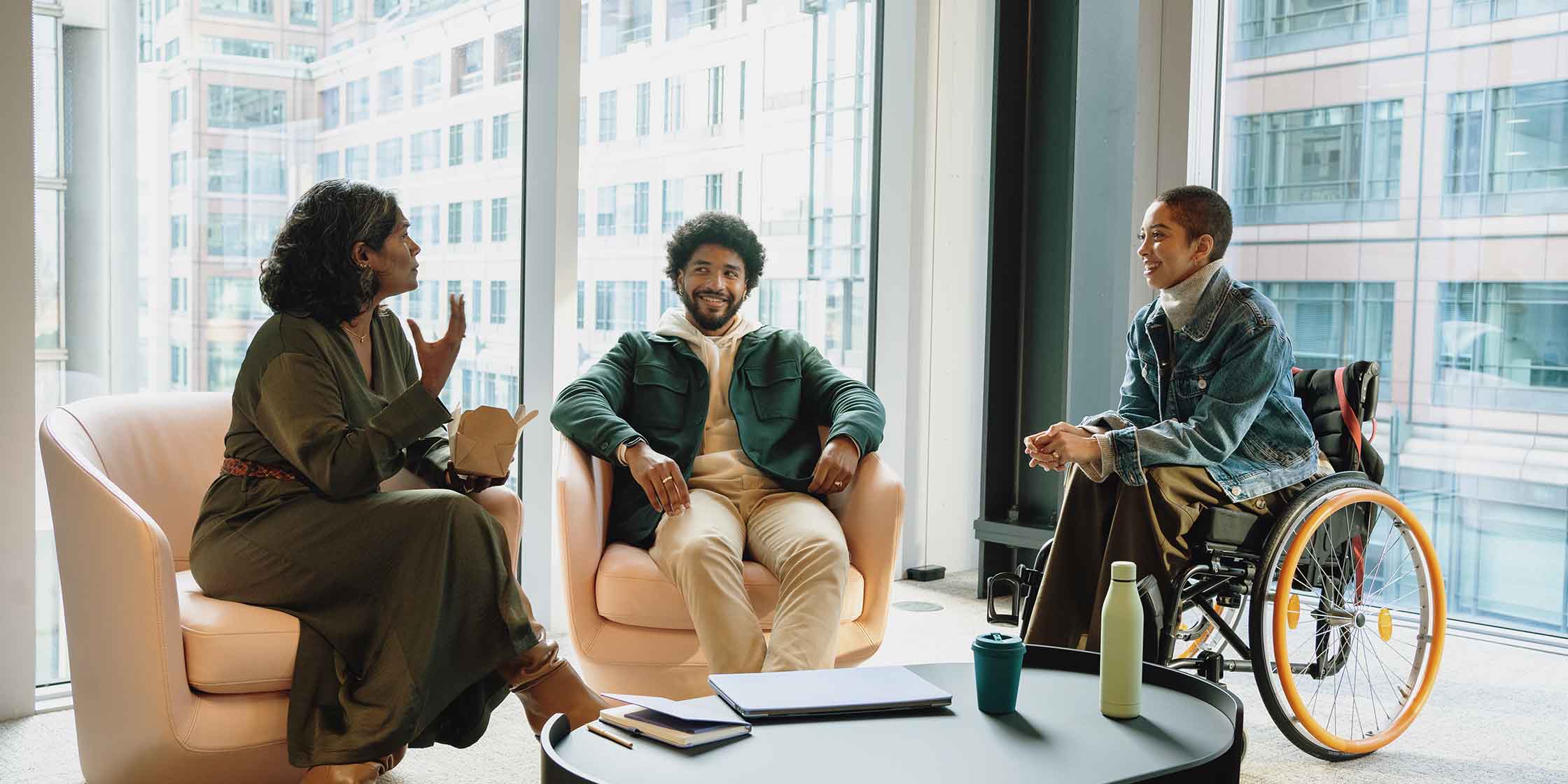 Three coworkers sitting in a corner office and chatting.