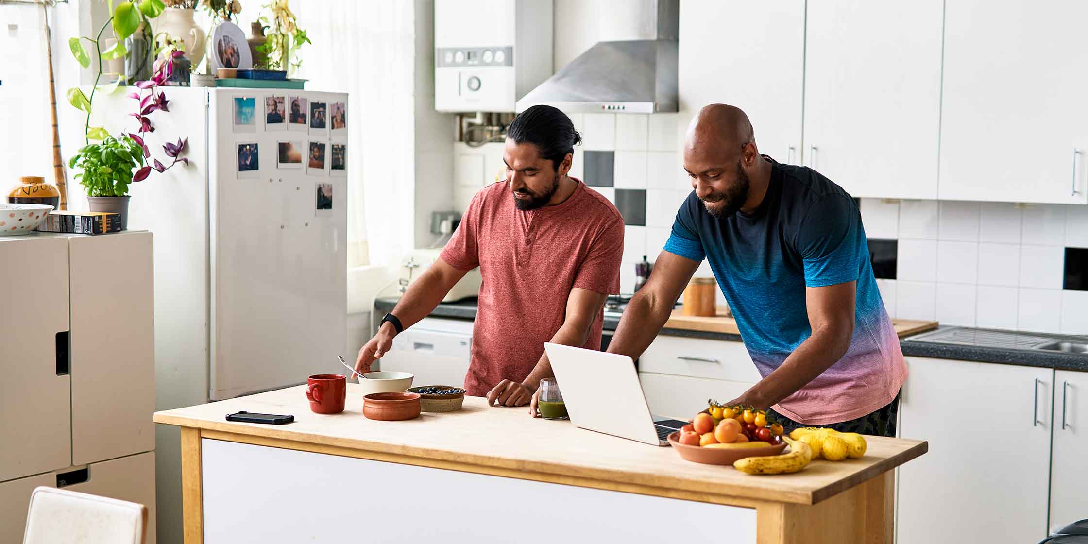 A couple is in the kitchen. One person prepares food while the other consults