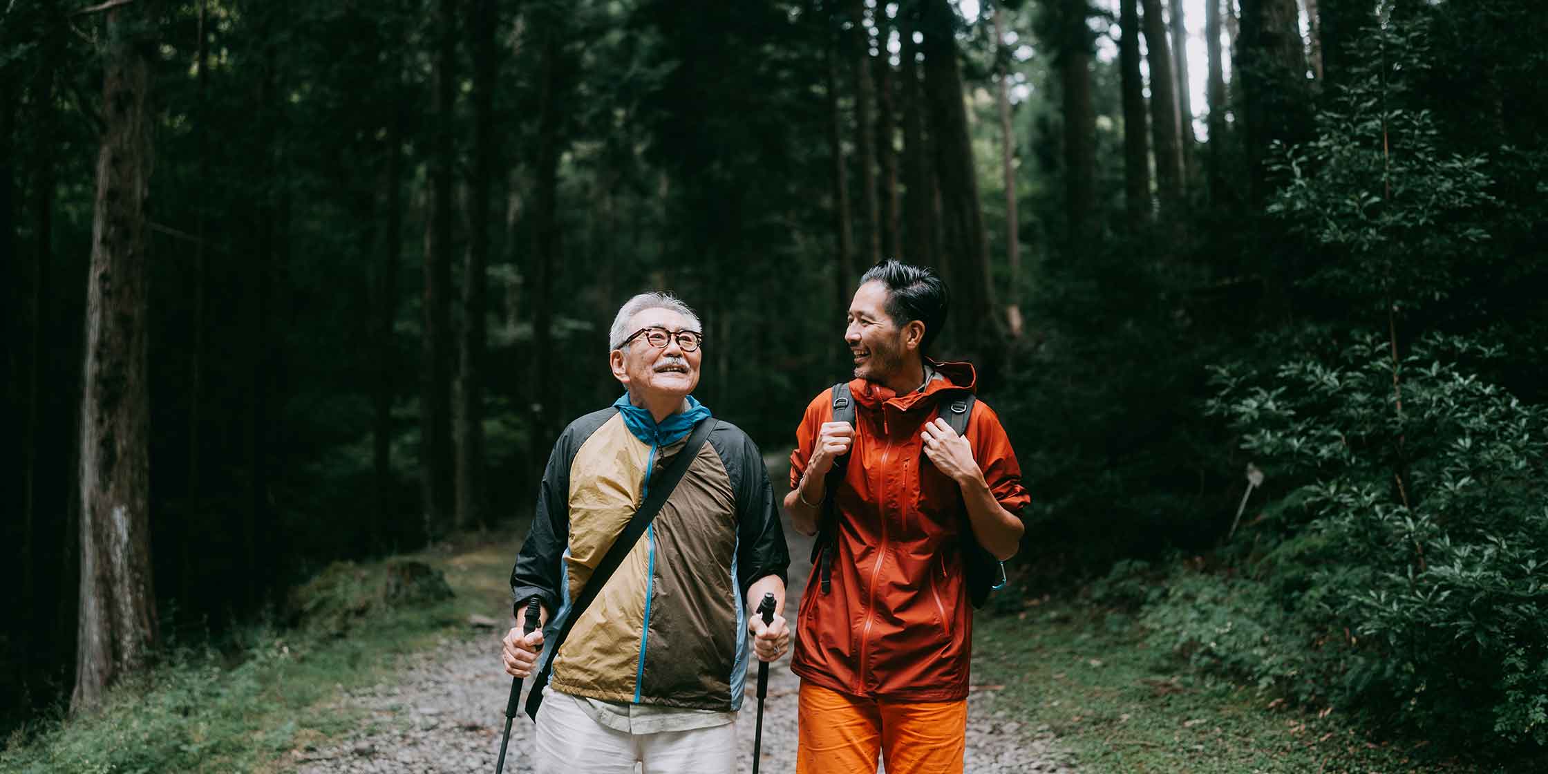 Two people hiking on a trail through the woods.