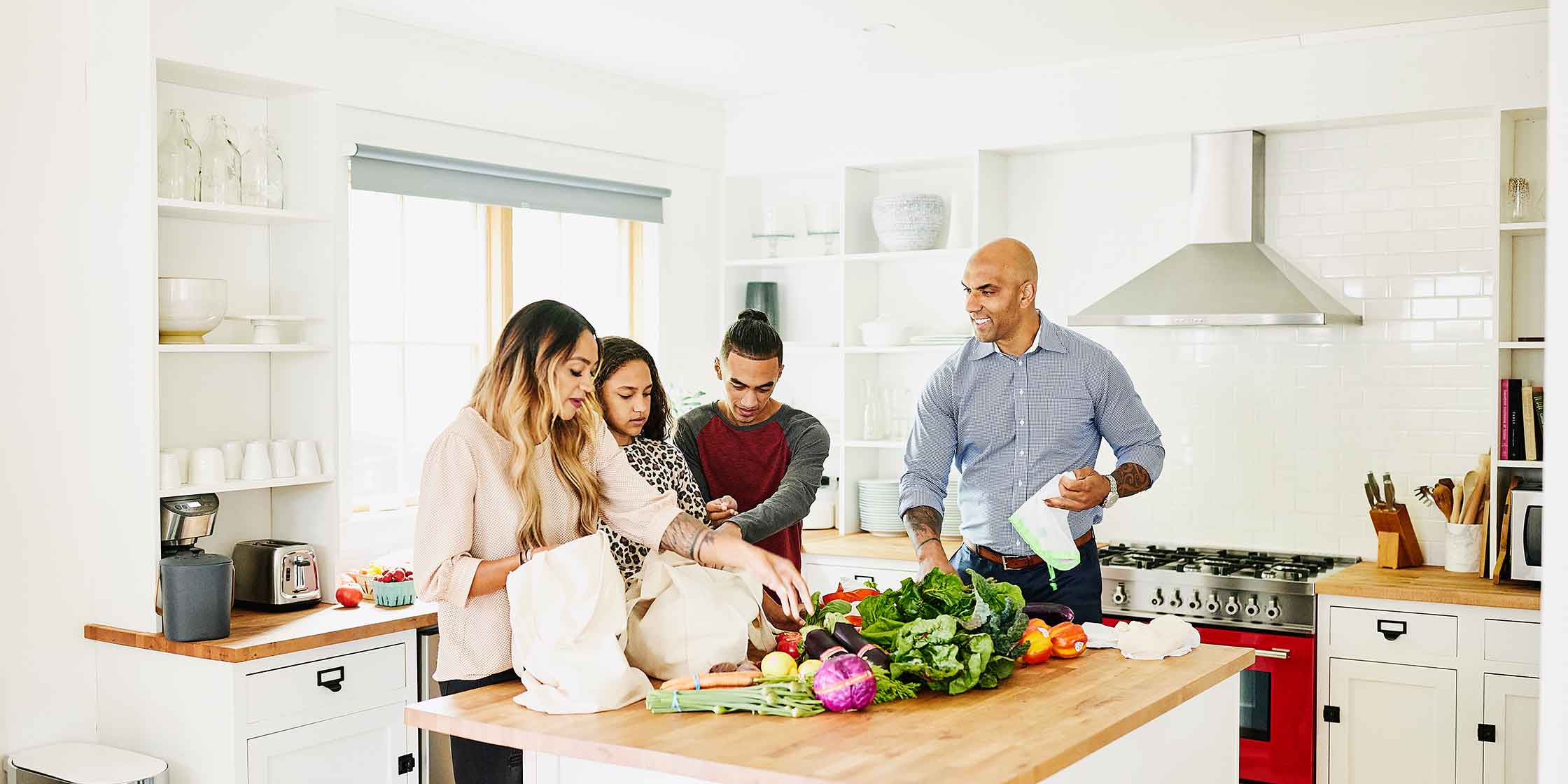 A family of four unloads groceries, one of their ongoing monthly expenses, onto their kitchen counter.
