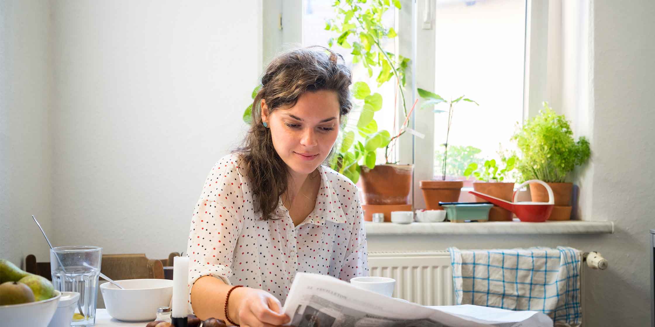 A person reads a newspaper at a kitchen table.