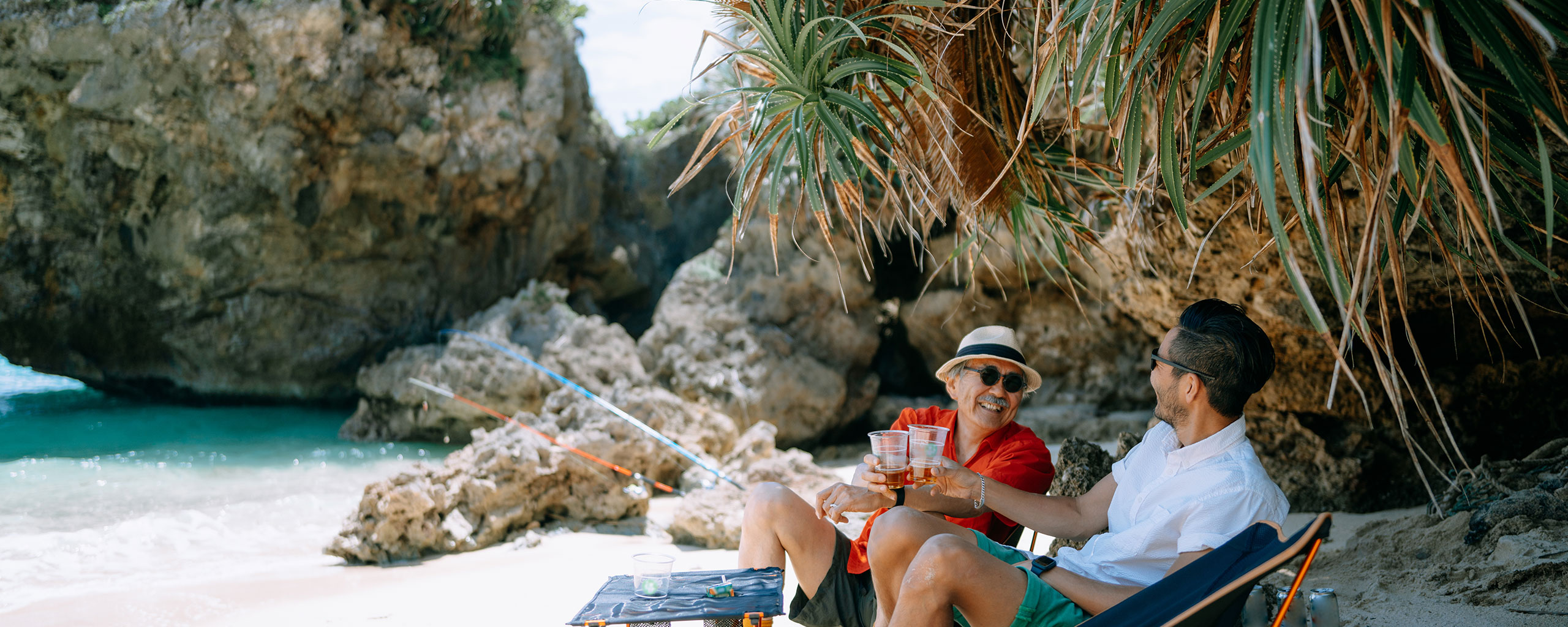 Two people raise glasses on a beach while on vacation.